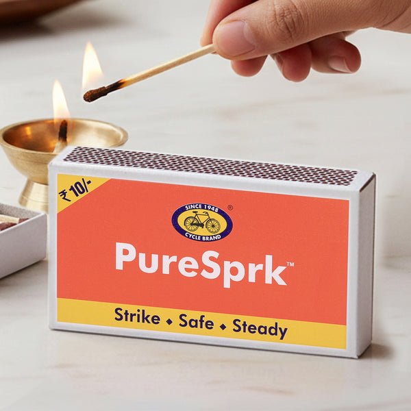 Person lighting a match from a box of PureSprk matches on a light background